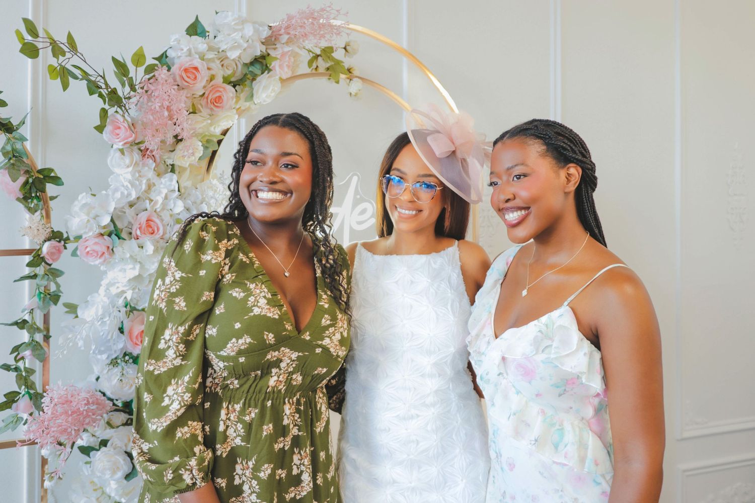 Three women smiling and celebrating together in front of a floral backdrop at a bridal shower in Calgary