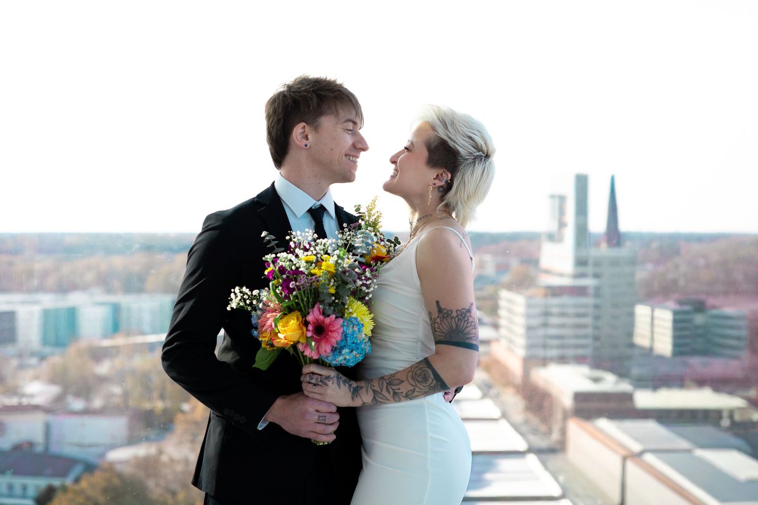 A romantic wedding couple shares tender moments on a rooftop terrace with a city skyline in the background.