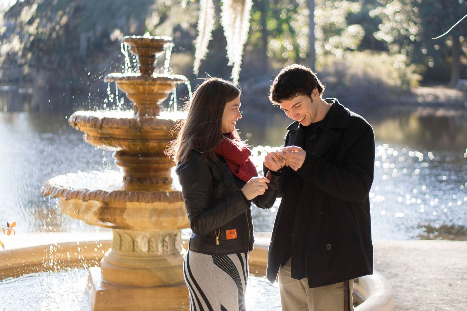 A couple shares a tender moment near a fountain in a park on a sunny winter day.
