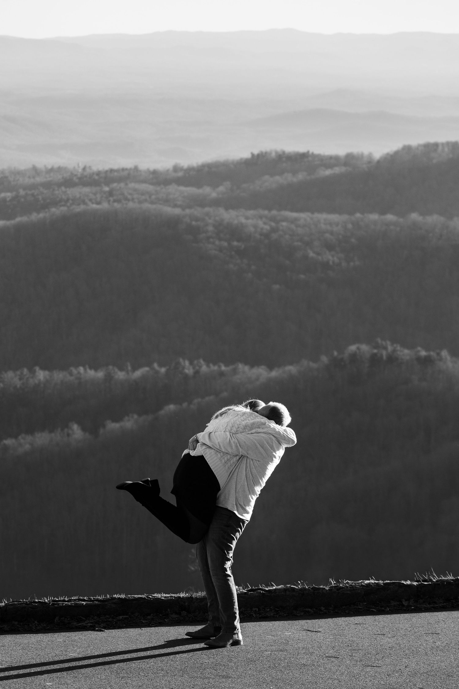 A silhouette of a person bending forward against a mountainous landscape in black and white.