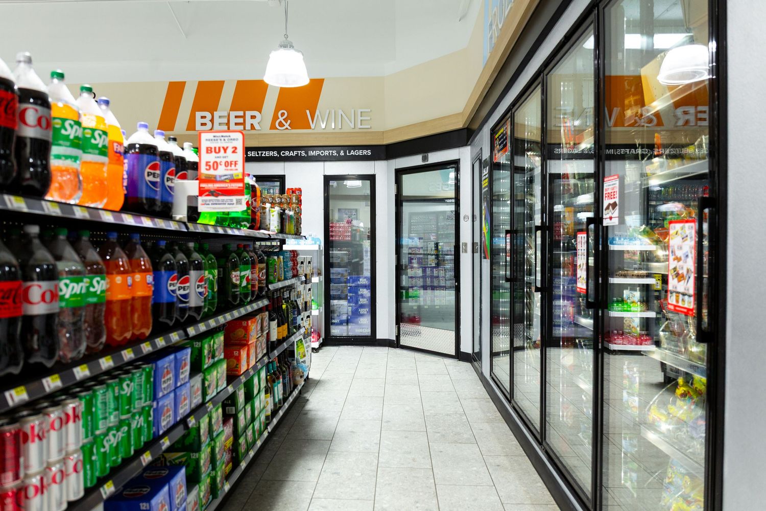 Long grocery store aisle with refrigerated cases and shelves stocked with beverages and food items.
