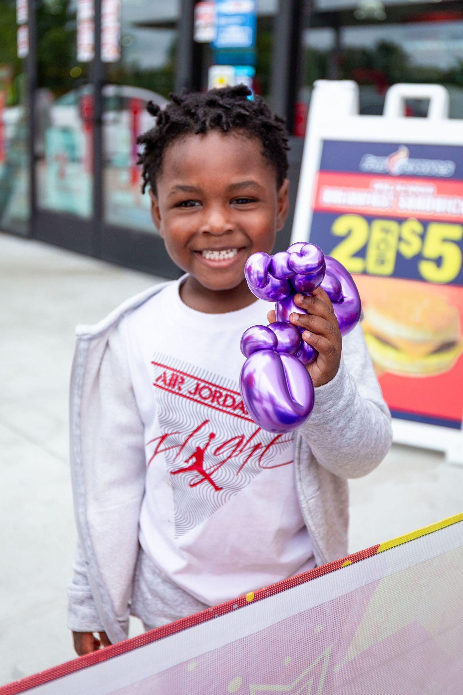 A child wearing a white Air Jordan sweatshirt smiles while holding purple decorative elements.
