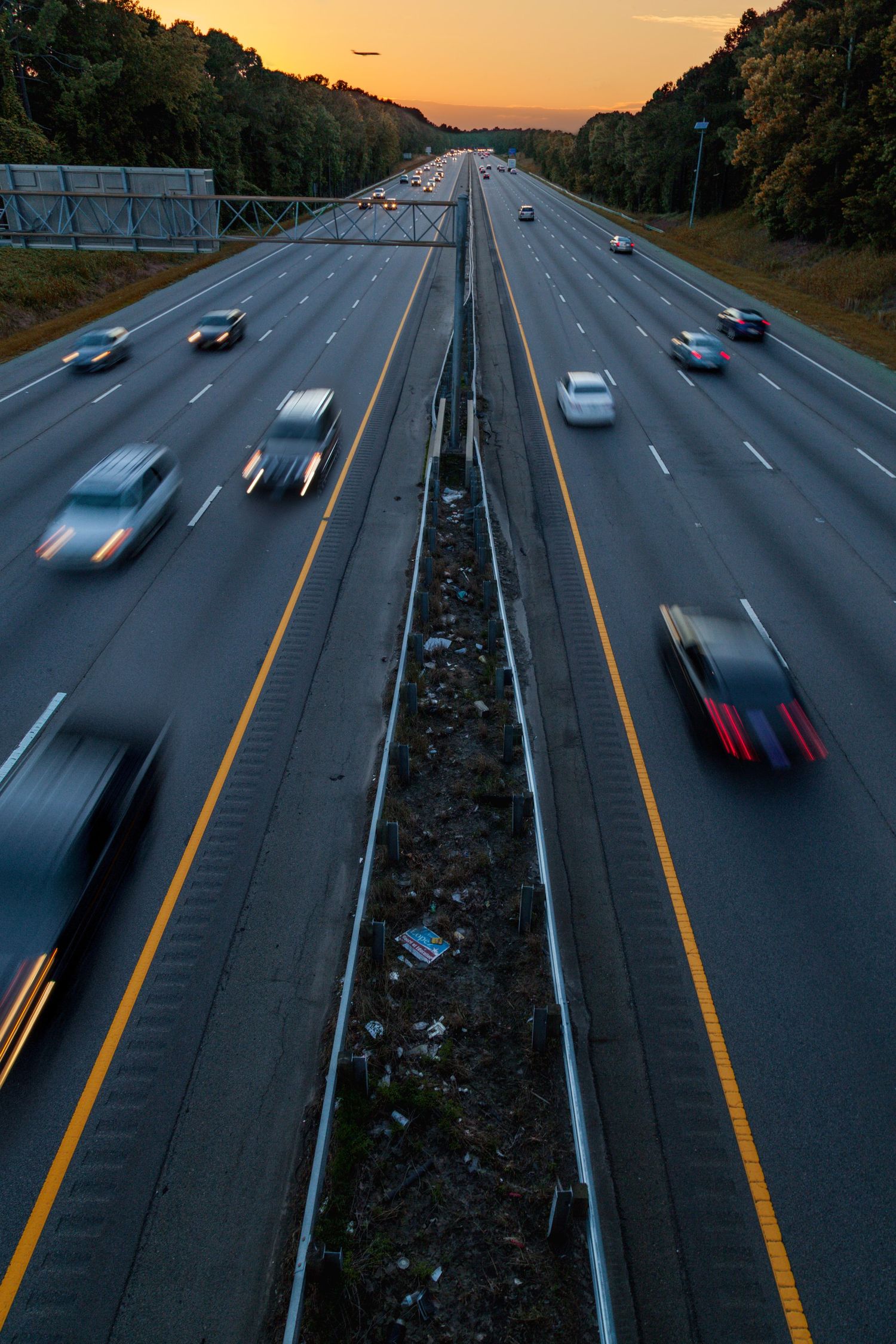 Long exposure shot of busy multi-lane highway at dusk with motion-blurred cars and warm orange sunset sky.