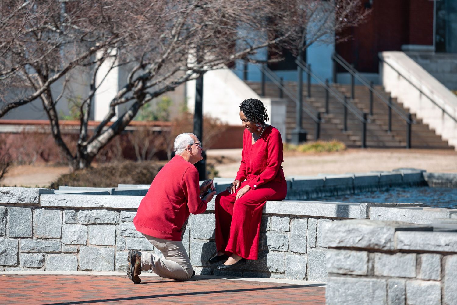 Two people in red jackets sit on stone steps during a winter day in an urban setting.