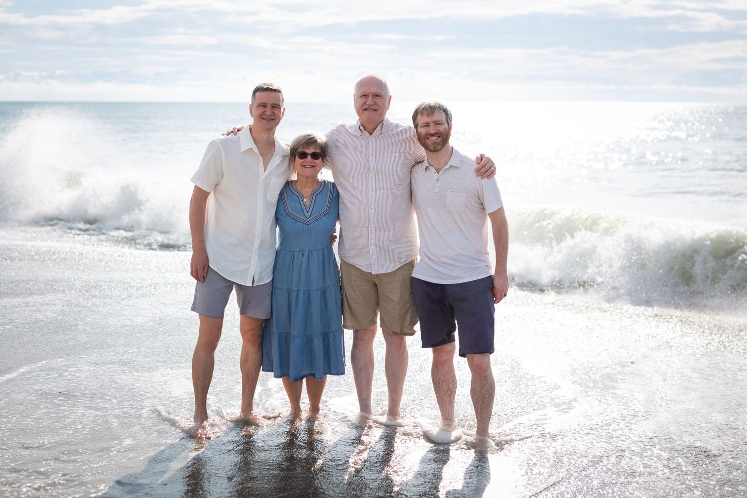 A family of four poses together at the beach with ocean waves crashing behind them.