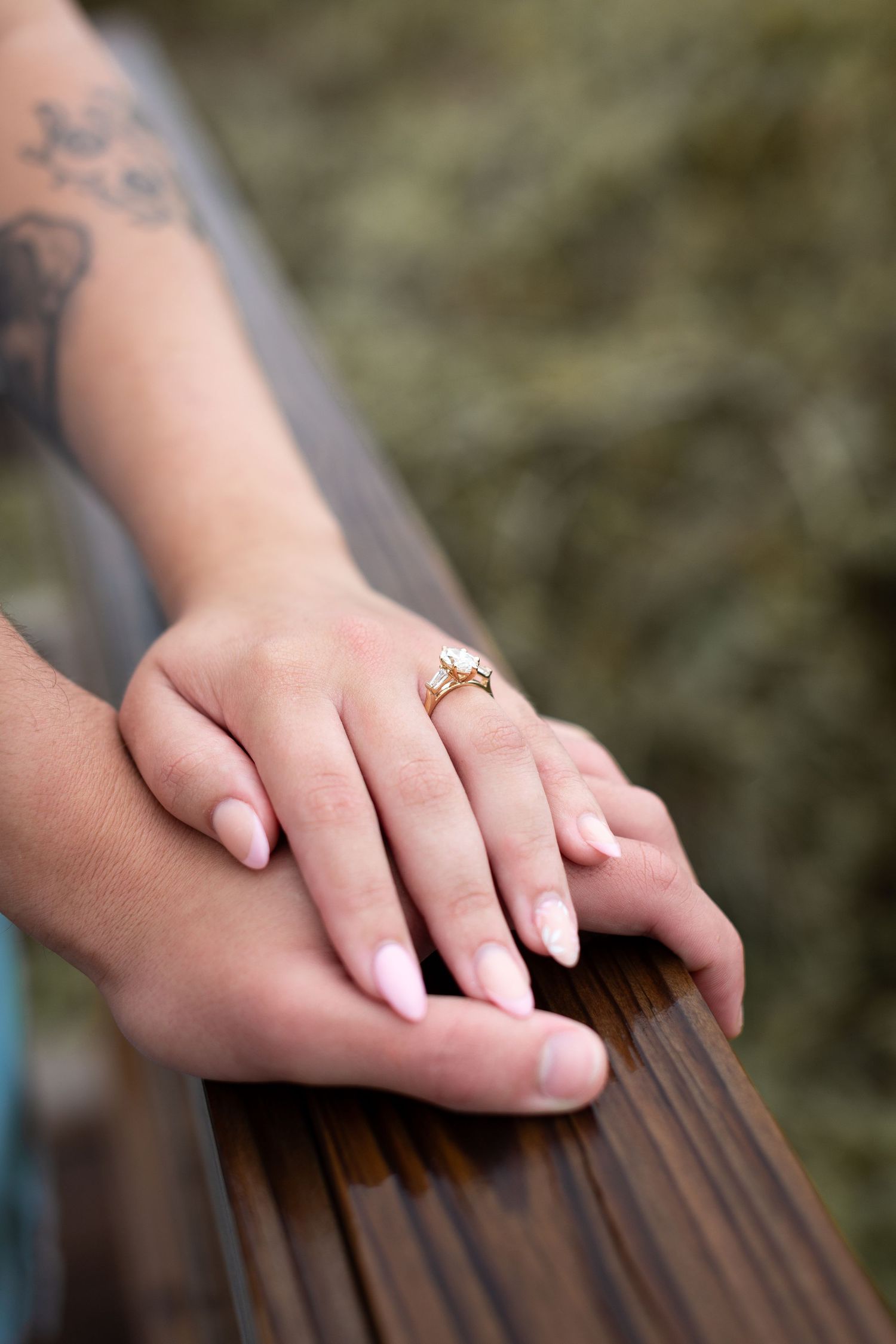 Close up of hands wearing a gold engagement ring resting on a wooden surface with blurred background.