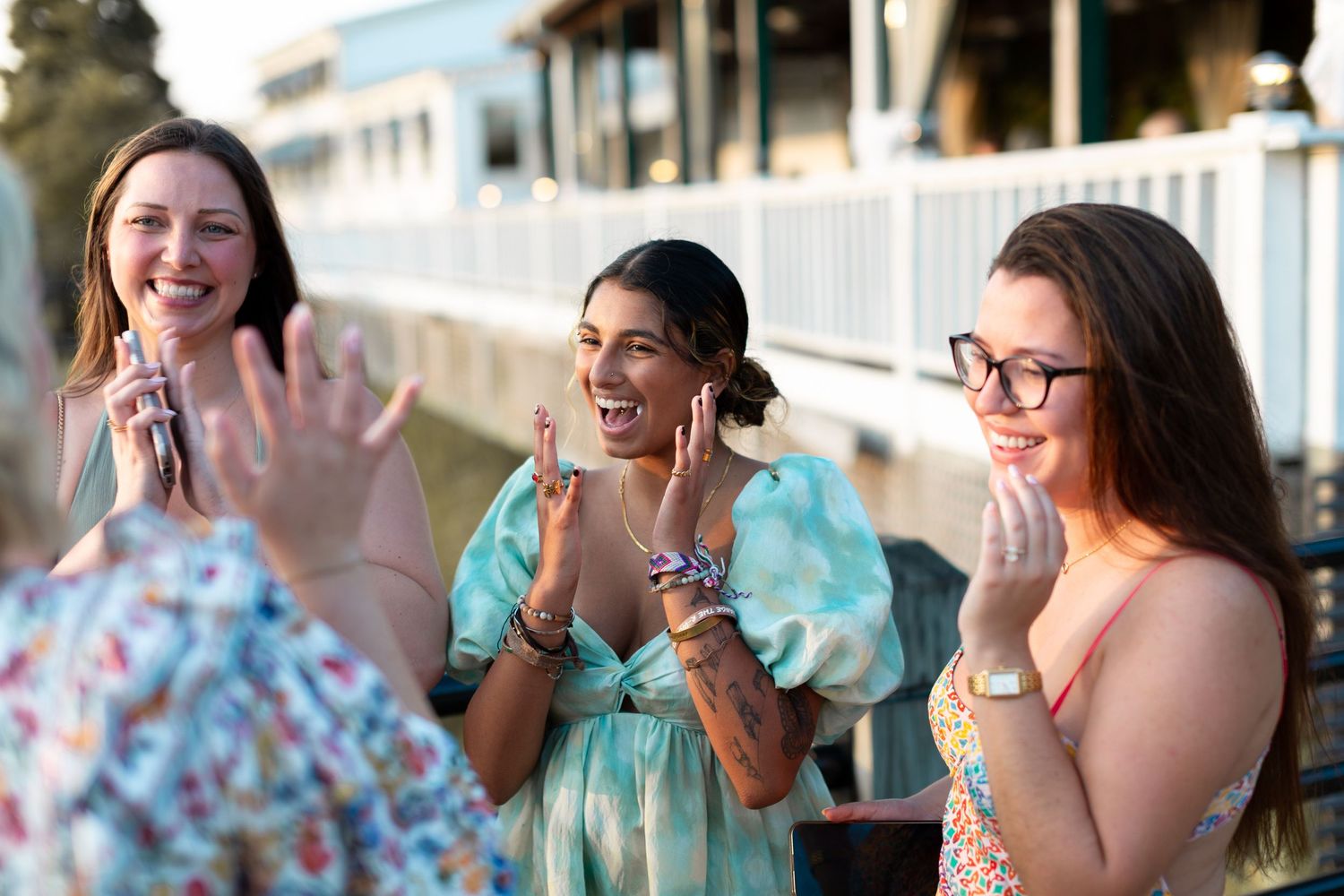 A group of friends laughing together at an outdoor gathering wearing casual summer attire.