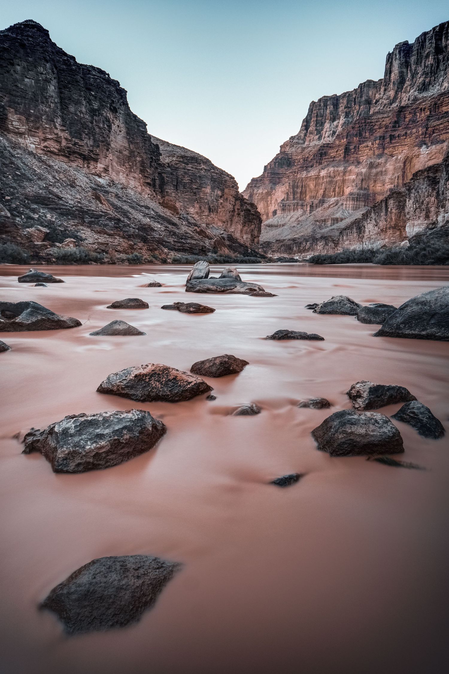 Silky pink Colorado River flows through rocky Grand Canyon landscape with smooth long-exposure water effect.