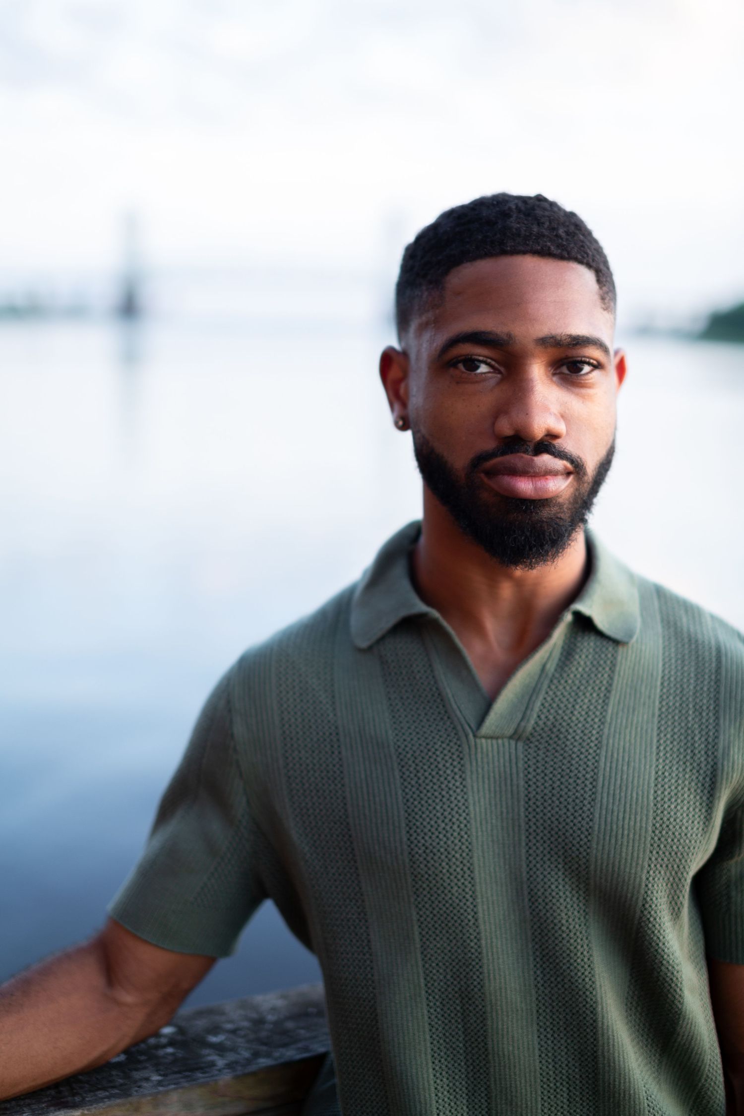A person in a sage green knit polo shirt poses against a blurred background.