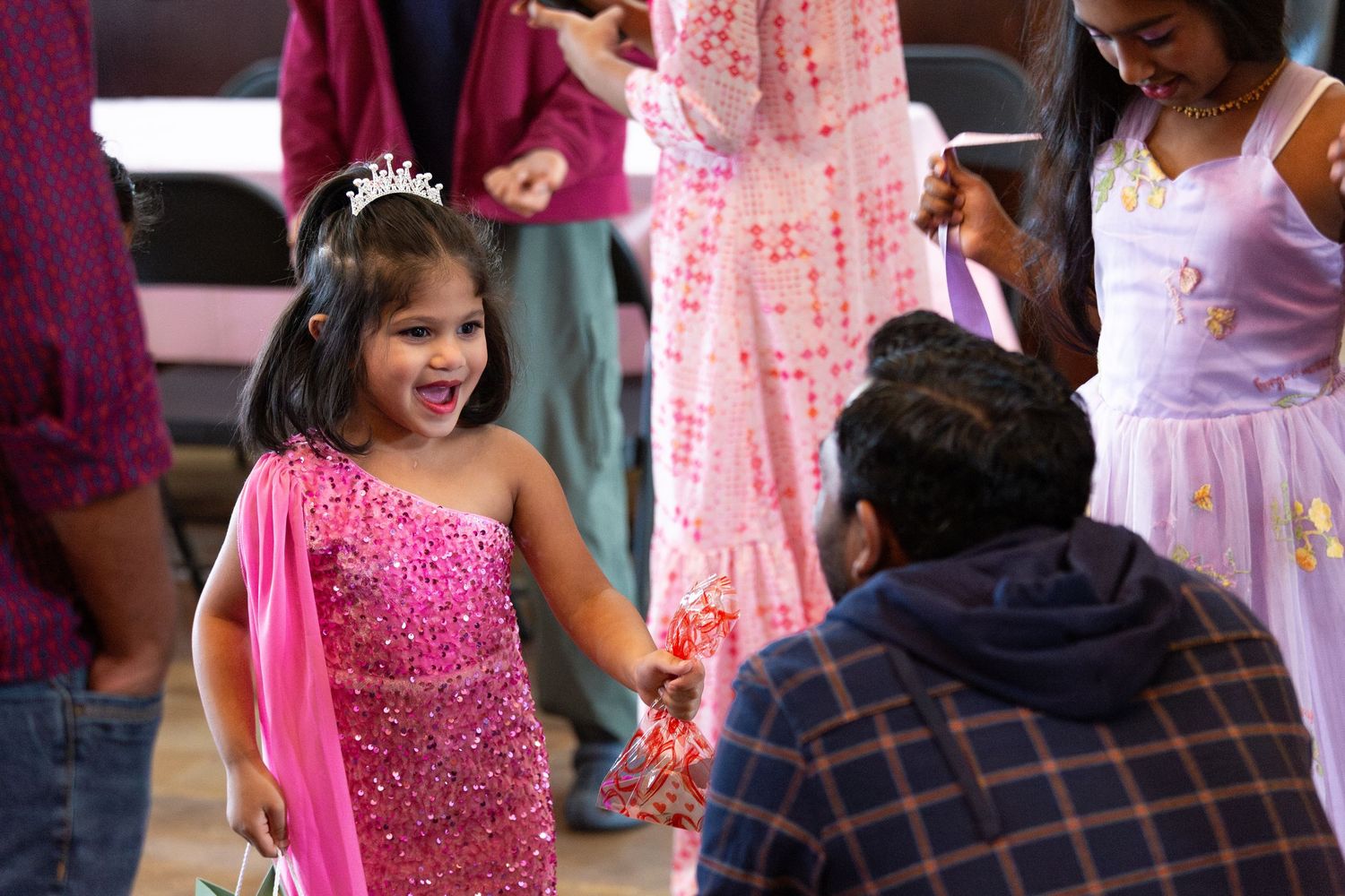 People in formal attire celebrate at an event with pink decorations and festive atmosphere.