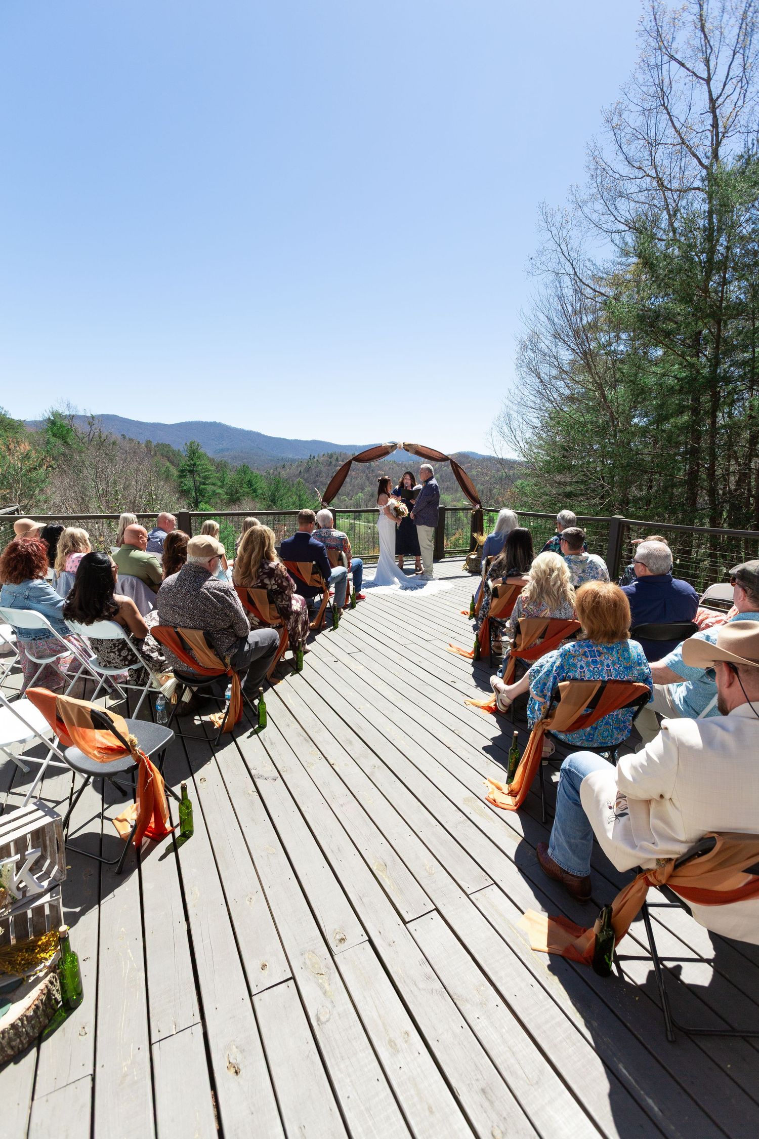 Musicians gather on a wooden deck in the mountains for an outdoor jam session with guitars and instruments.