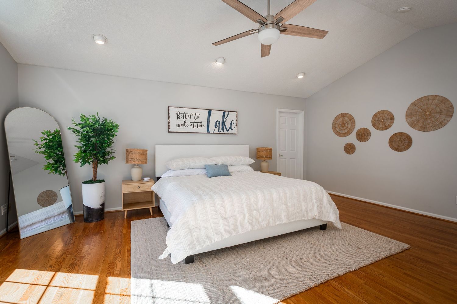 Spacious bedroom with hardwood floors, white walls, and natural light from multiple windows.
