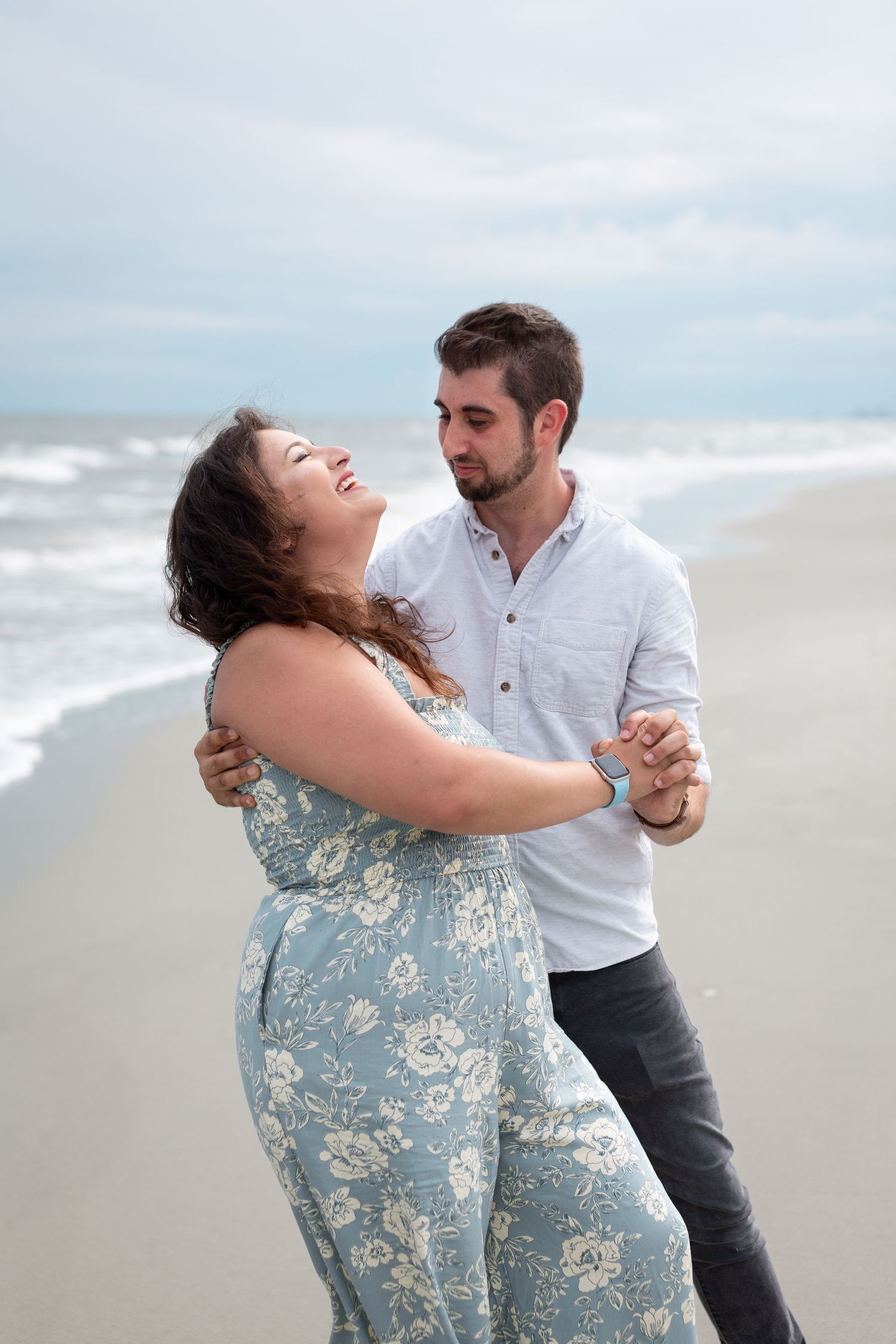 A couple shares a romantic dance moment together on a cloudy beach, with waves crashing in the background.