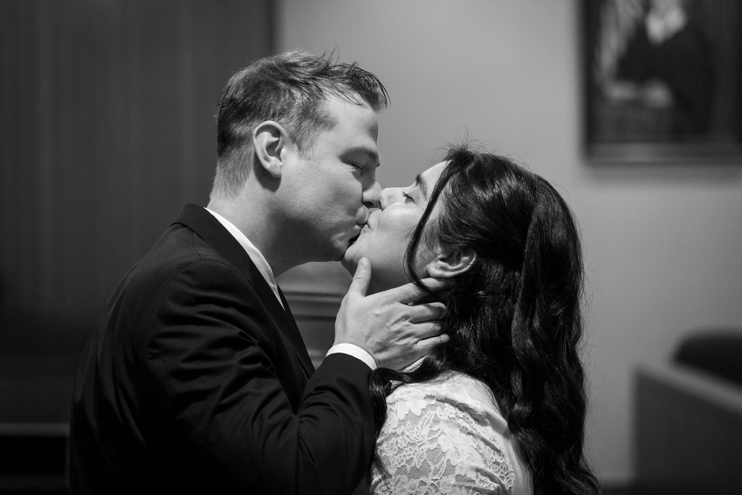 Black and white photo of a groom tenderly kissing his bride while cupping her chin during an intimate wedding moment.