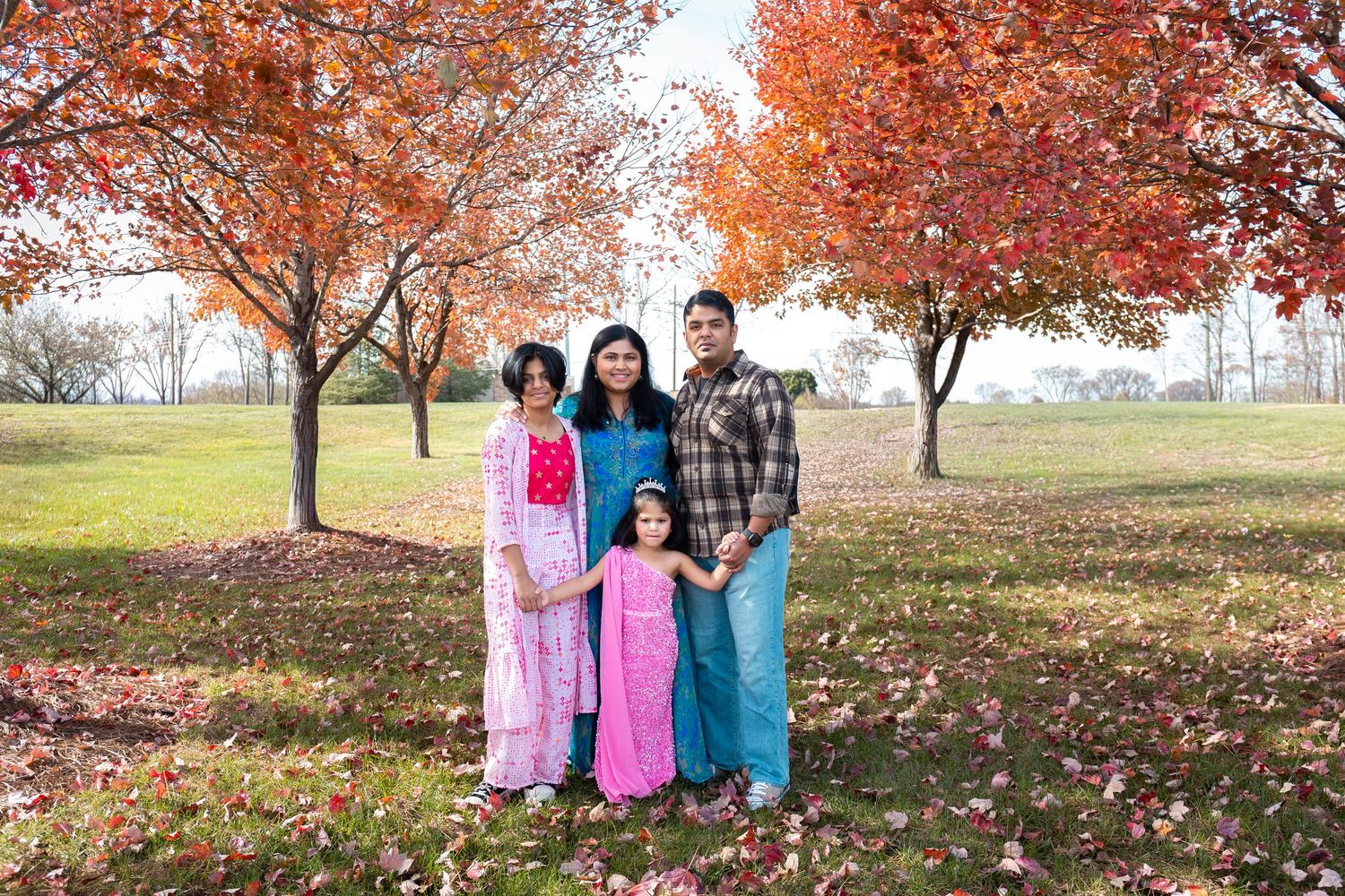 Family photo session in park with vibrant fall foliage and pink outfits.