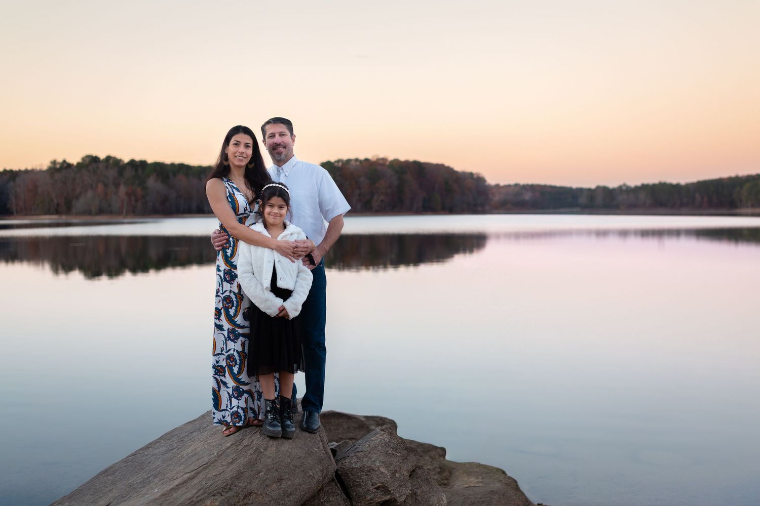 Family poses together on rocky outcrop overlooking serene lake at sunset.