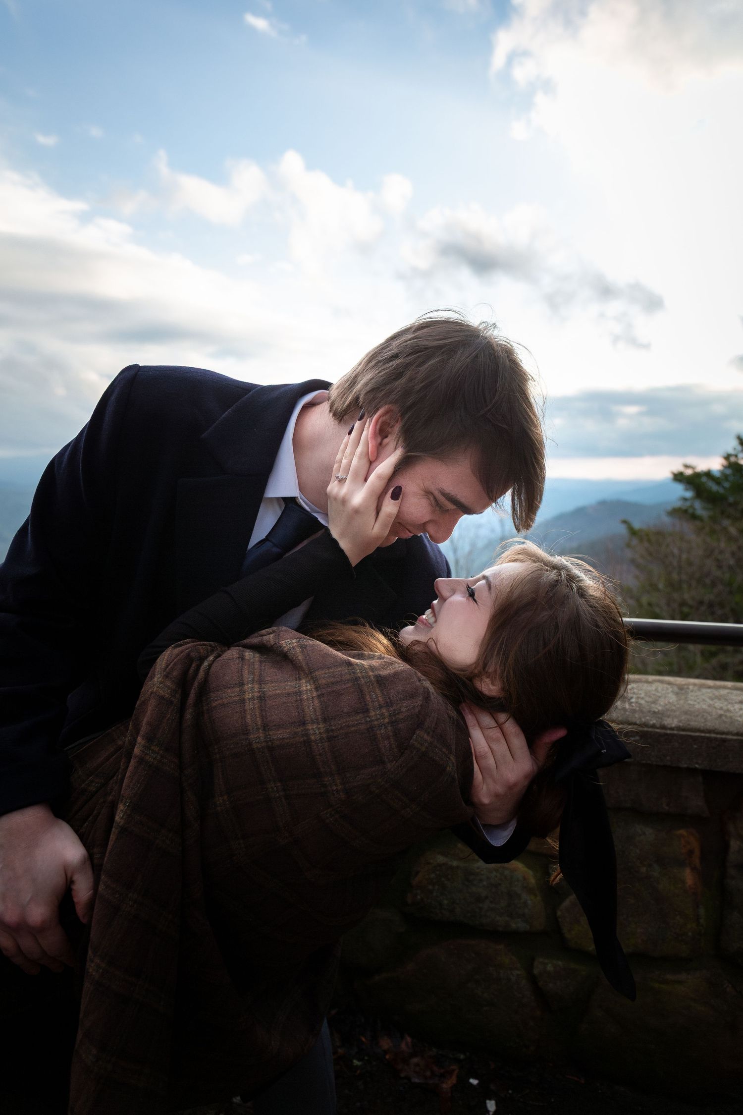 A romantic couple shares an intimate moment against a scenic mountain backdrop at sunset.