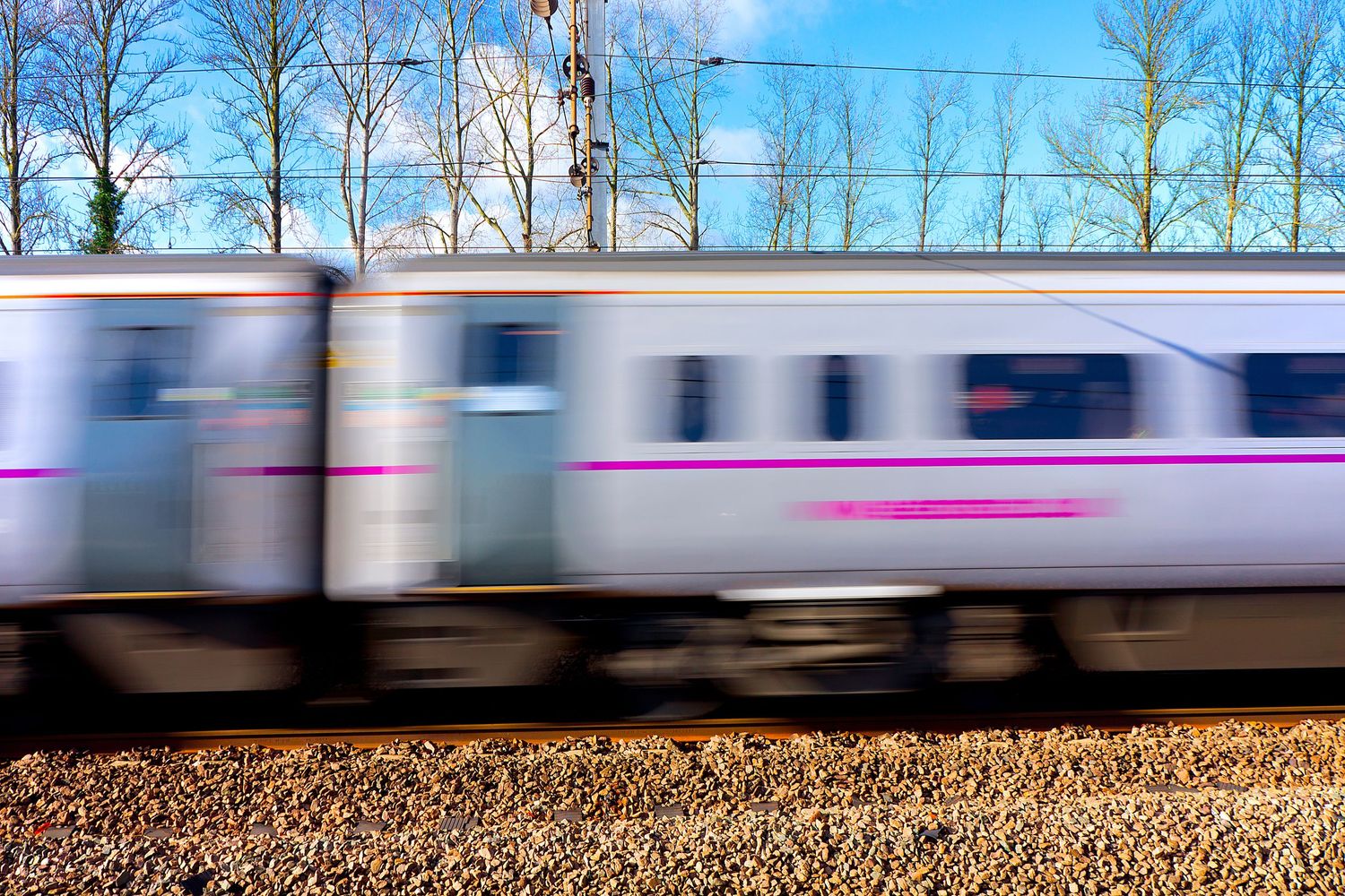 A speeding passenger train with pink accents captured in motion blur on a sunny day.