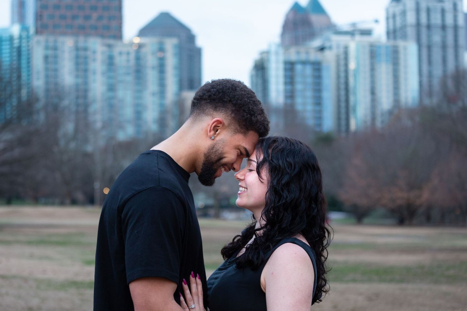 A couple embraces with the Atlanta city skyline and Piedmont Park in the background during golden hour.