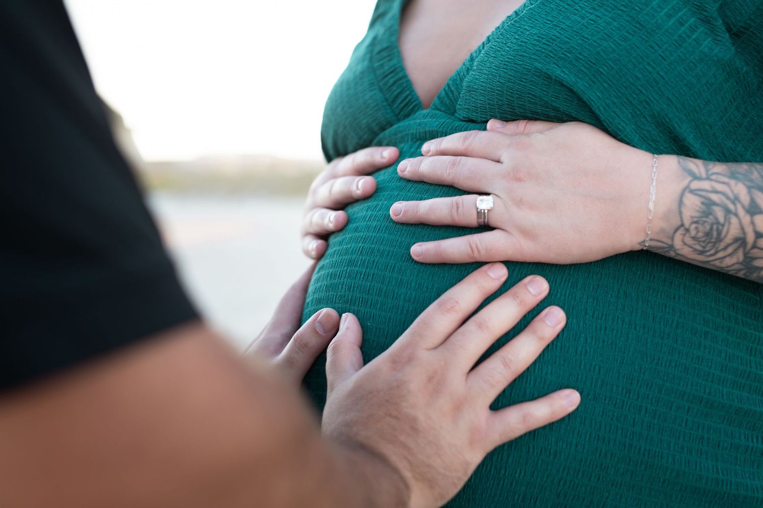 A close-up series of hands cradling a pregnant belly wearing an emerald green knit sweater.
