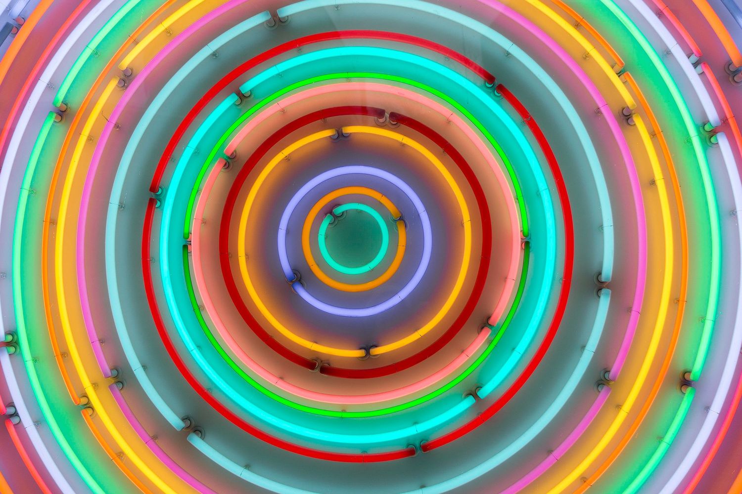 Colorful concentric neon circles creating a hypnotic spiral pattern with vibrant rainbow hues on a light background.
