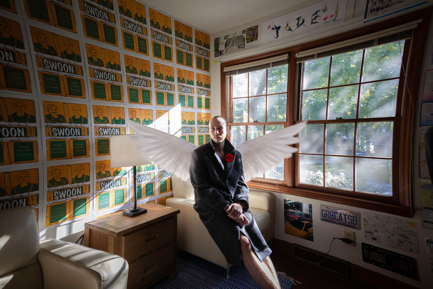 Person with angel wings sits in a room decorated with Oregon license plates on the walls near a window.