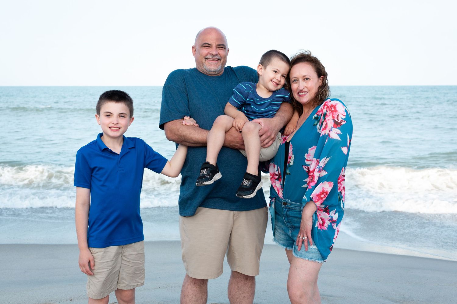 Family enjoying a sunny day together at the beach with waves and sand in the background.