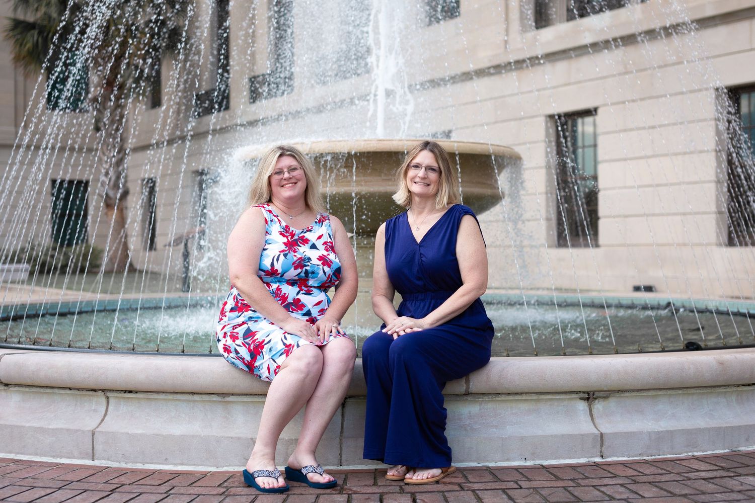 Two people sit by ornate stone fountain in urban setting.