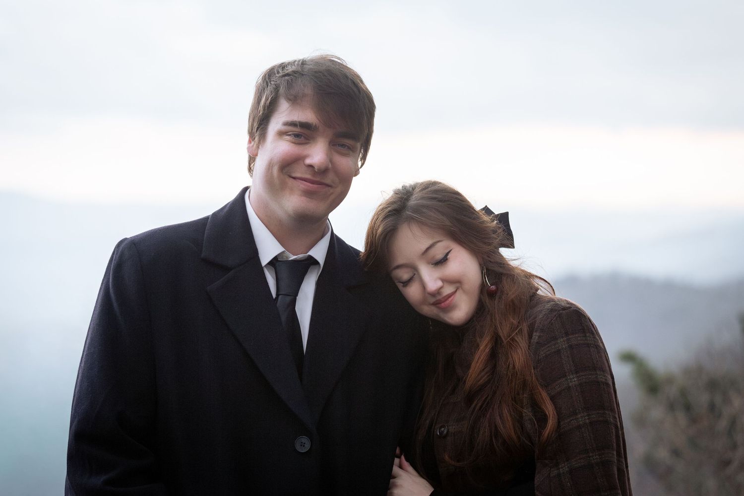 A couple in formal attire share an intimate moment together on a misty mountainside overlook.