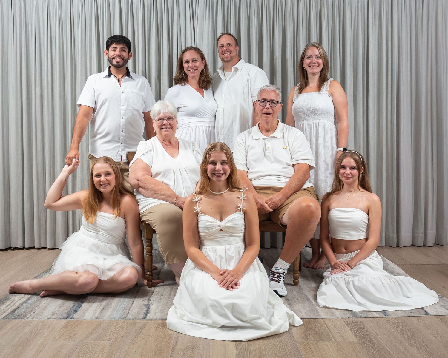 A group in coordinated white outfits poses together against a gray curtain backdrop for a formal portrait.