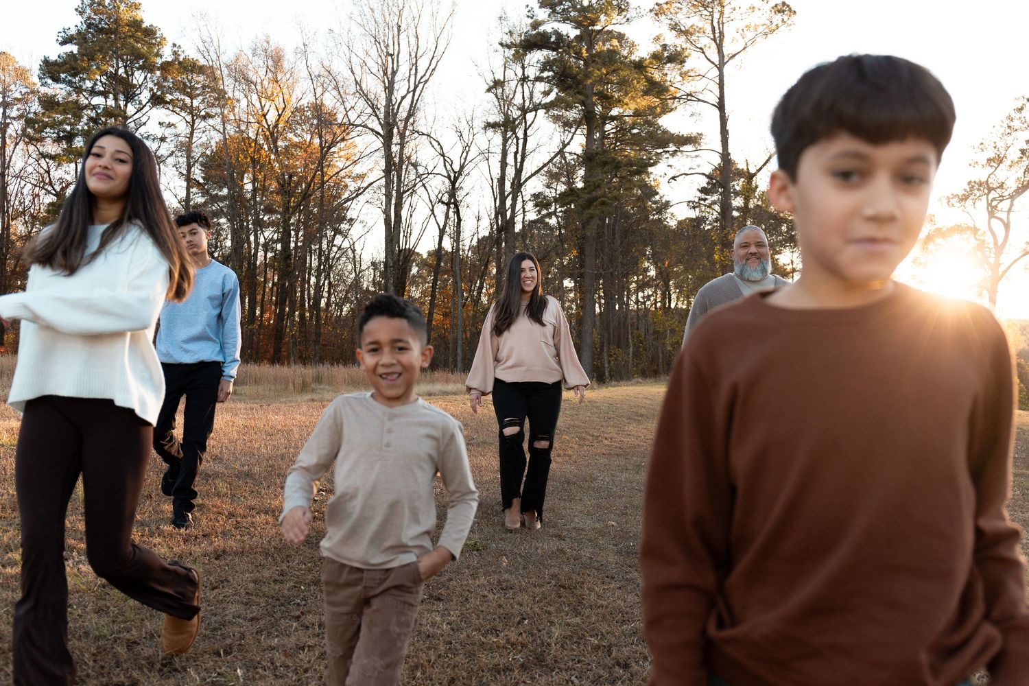 Family group walking outdoors in a sunlit park during autumn, with children and adults enjoying a casual stroll.