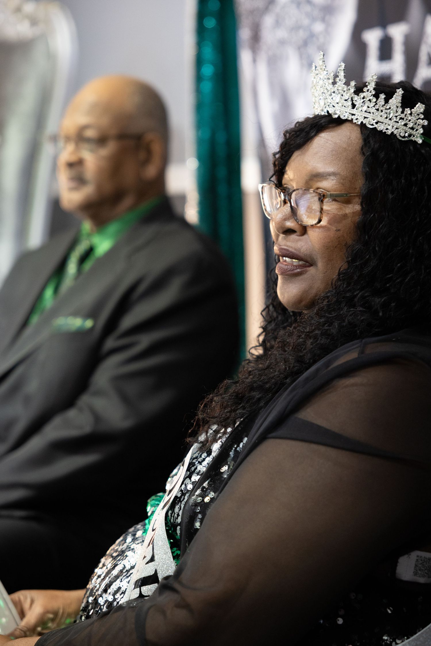 People in formal attire seated at an event wearing crowns and festive accessories.