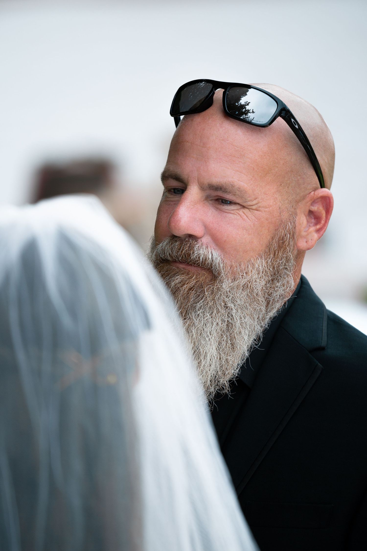 Close-up profile view of a man with a gray beard wearing sunglasses and dark clothing.