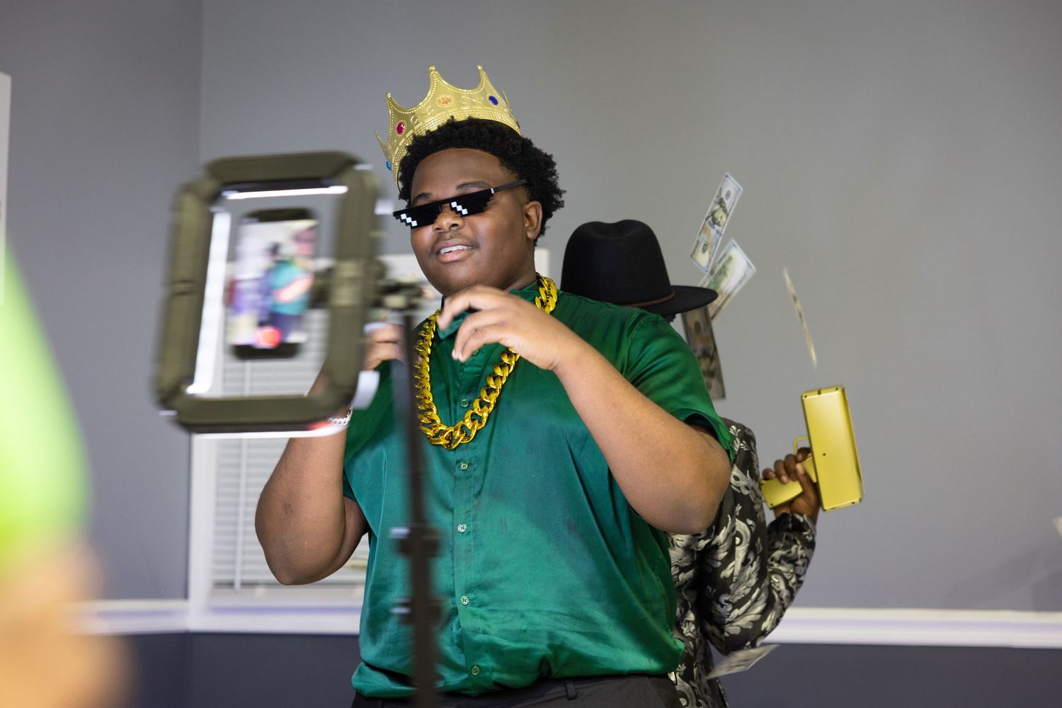 Person in green shirt wearing crown and sunglasses with festive decorations.