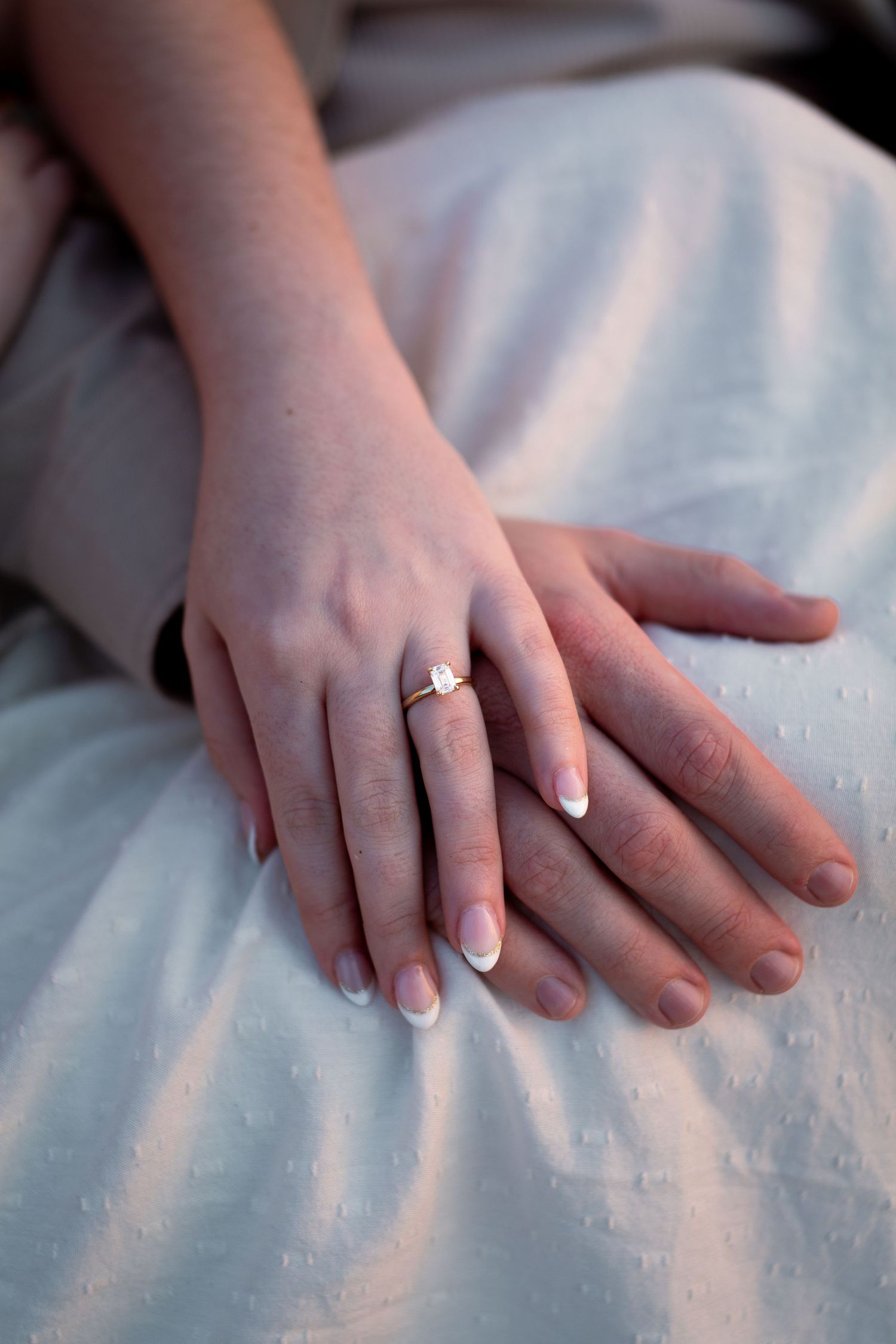 Close-up sequence of hands showing engagement ring on finger against white fabric background.