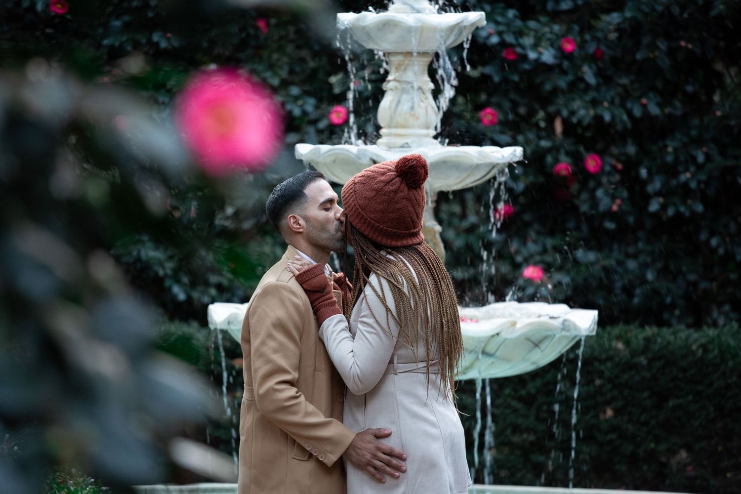 Two people share an intimate moment in a snowy winter garden with pink decorative elements.