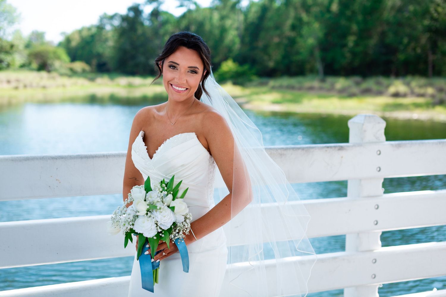 Bridal portraits taken on a white fence bridge over water on a sunny day.