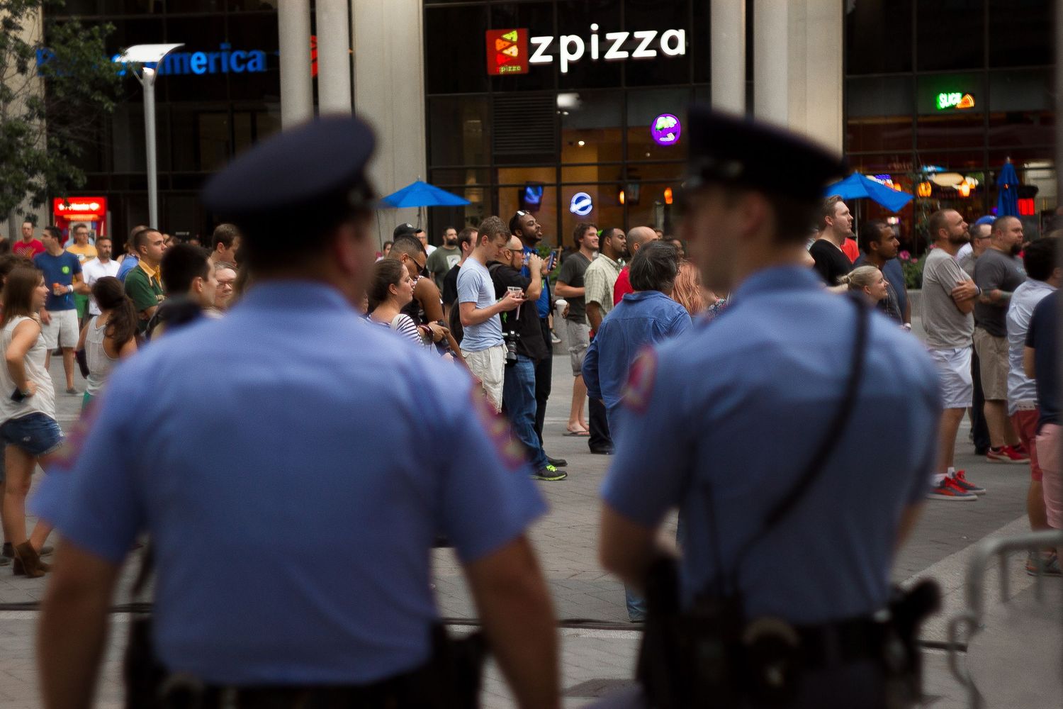 Police officers patrol a crowded city street during an outdoor event with neon signs visible in the background.