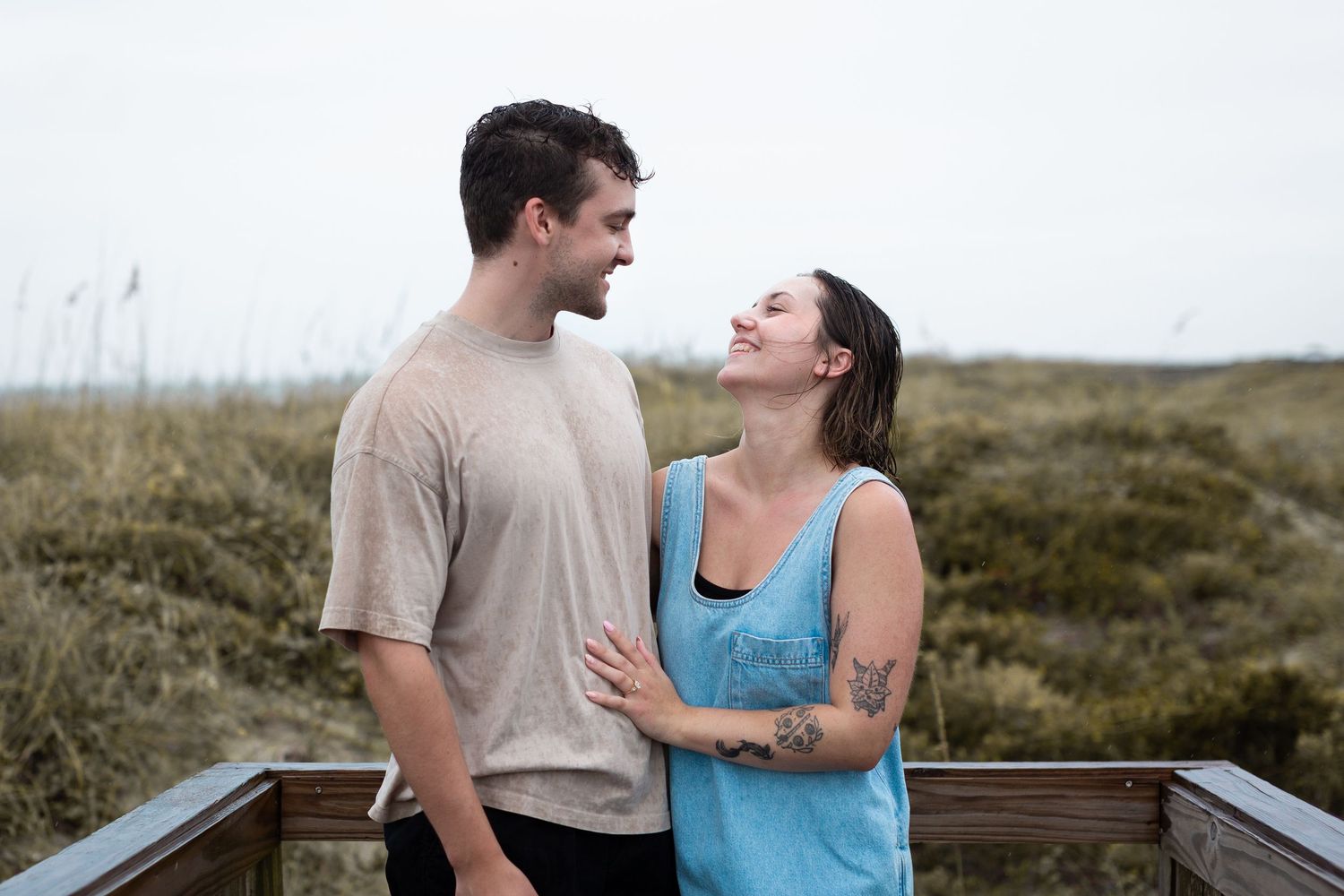 A couple in casual attire shares a romantic moment together on a wooden deck overlooking a scenic landscape.