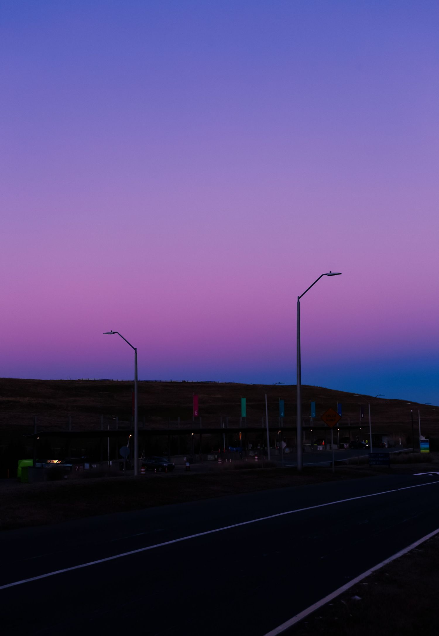 Scenic purple and pink gradient sunset sky over a road with street lamps at dusk.