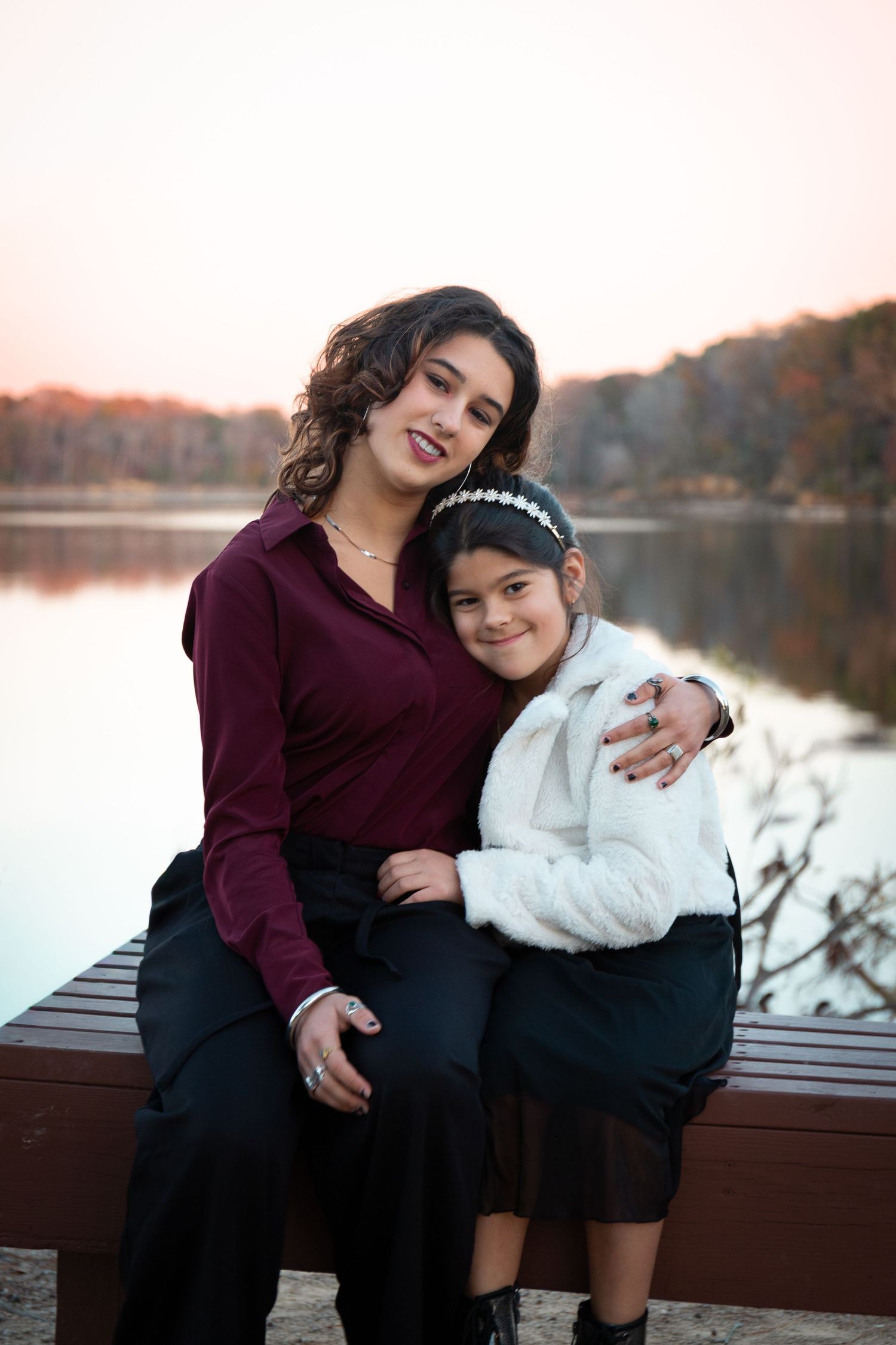 Two people sitting close together on bench by lake during autumn sunset.