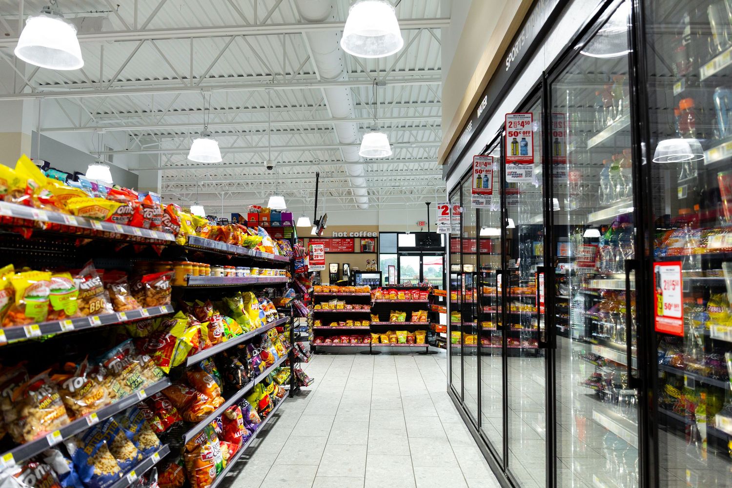 A grocery store aisle with fully stocked shelves of snacks and bright fluorescent lighting overhead.