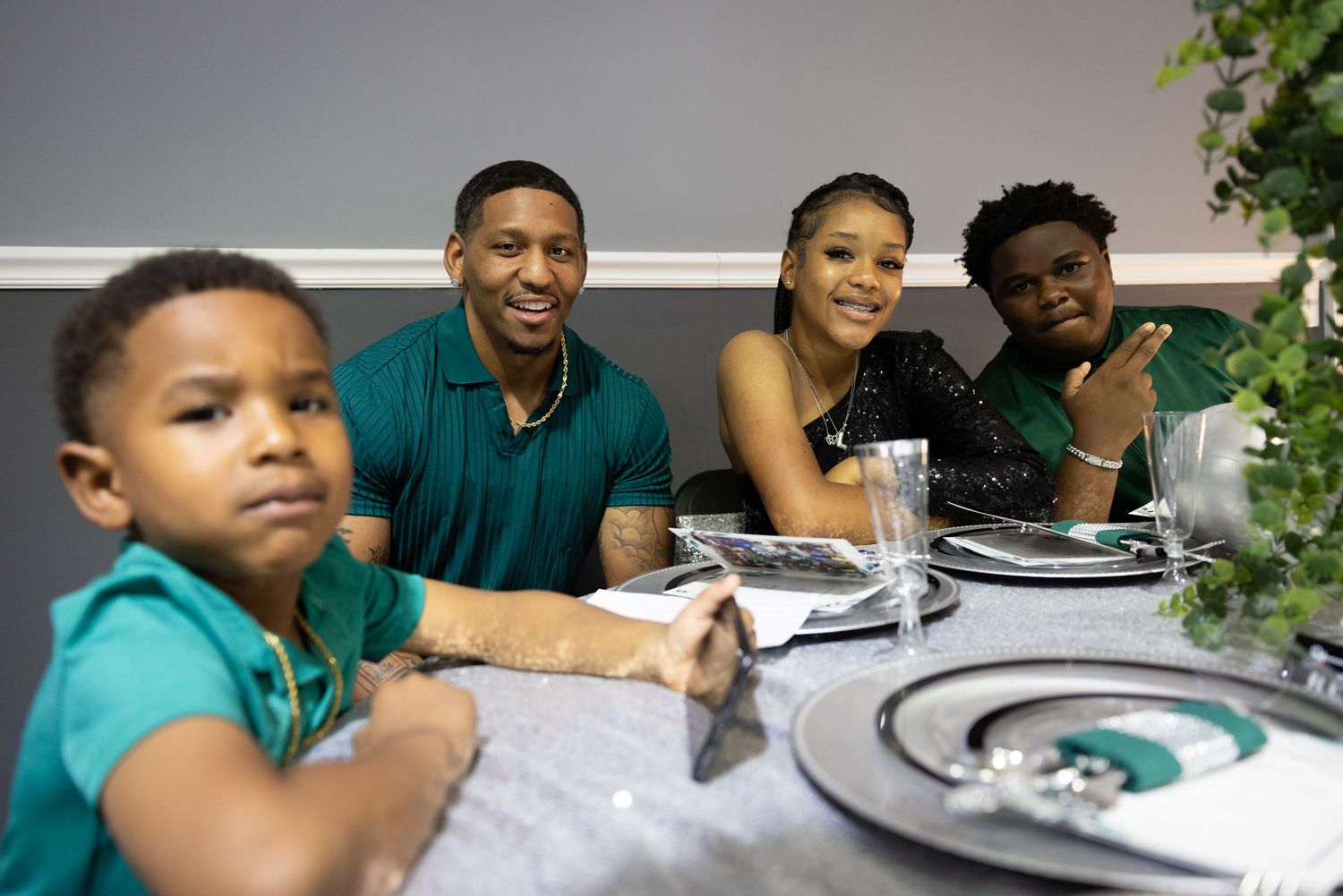 Group of people in teal shirts seated around dining tables at a community gathering.