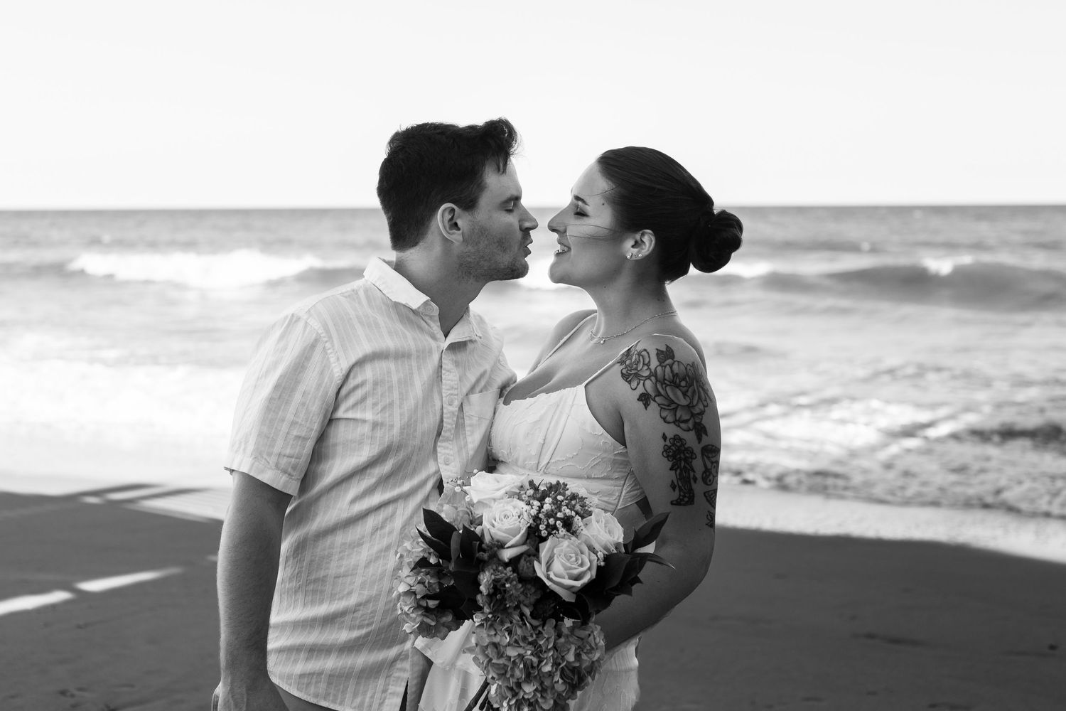 A romantic black and white beach photoshoot with gentle waves crashing in the background.