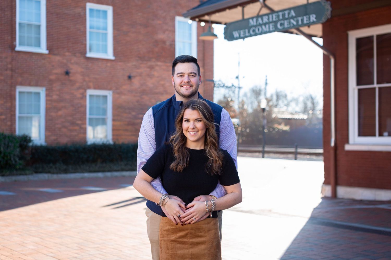 Couple posing together in front of Marietta Welcome Center on a sunny day.