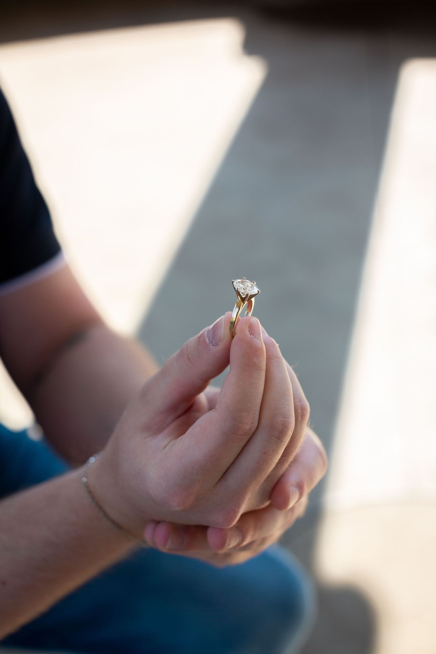 Hands holding and examining a delicate engagement ring in natural lighting.
