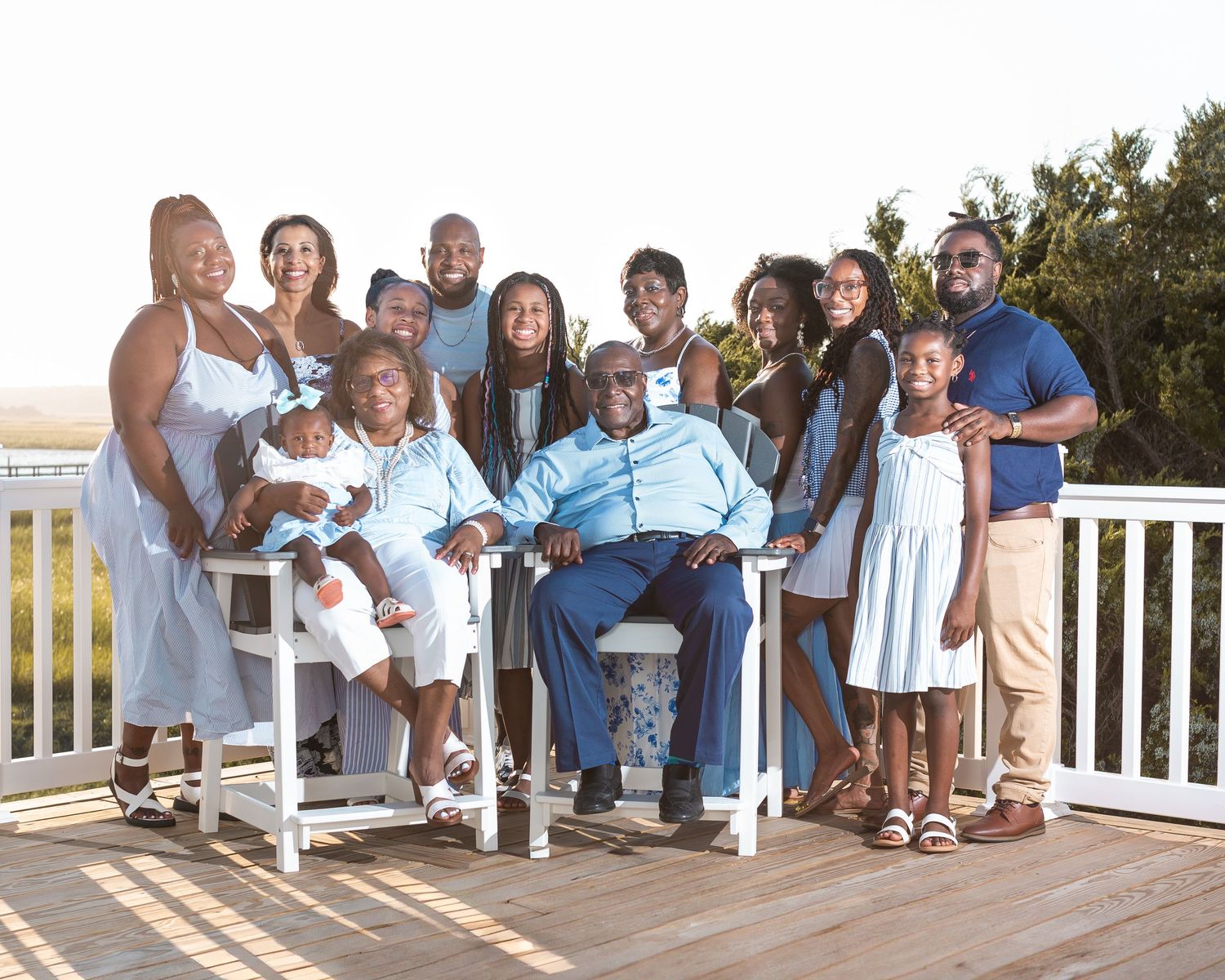 Extended family group in coordinating blue and white outfits sits together on wooden deck steps.