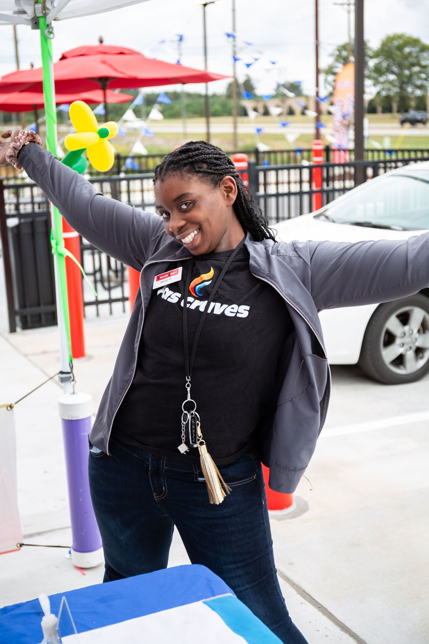 Person in black top celebrating with arms raised at outdoor venue with red umbrellas and colorful decorations.