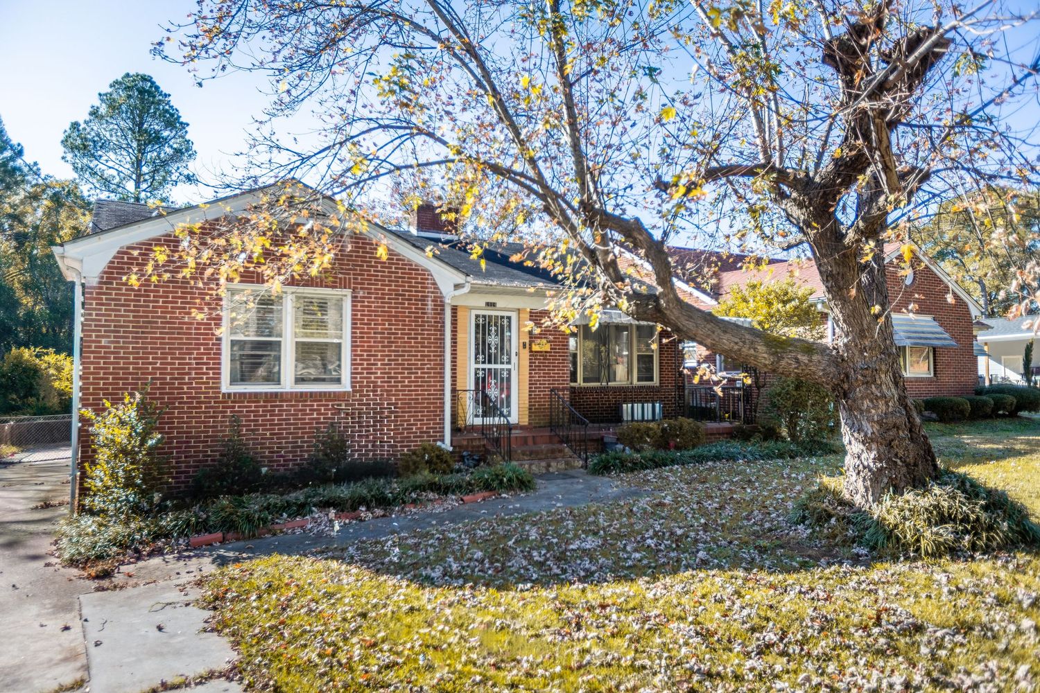 Panoramic view of a residential property with fallen leaves and mature trees in the yard.