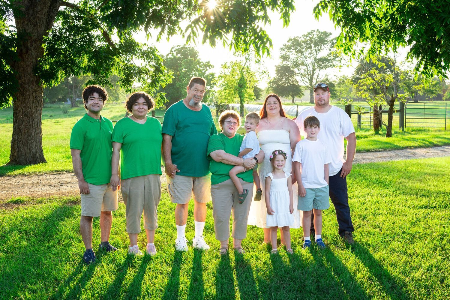 Large family group in green and white shirts posing together on a sunny grassy lawn surrounded by trees.